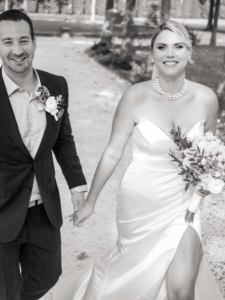 Srećan par, obučen u elegantne venčane odevne kombinacije, šeta putem u vili Viko. Mladoženja u crnom odelu, a mlada u prelepoj venčanici. Njihove ruke su isprepletene u znaku ljubavi i zajedništva. Lepa venčana buket i biserne ogrlice doprinose romantičnoj atmosferi. Ovo je trenutak koji će zauvek ostati zapamćen.